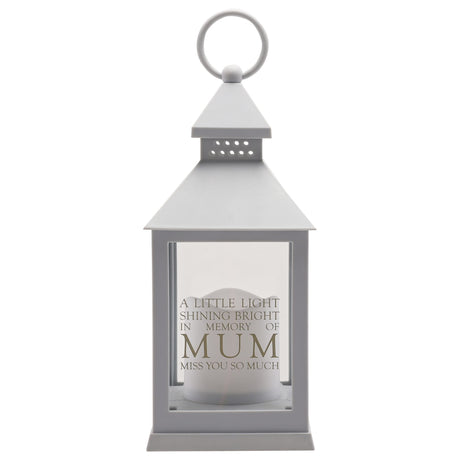 Grey metal graveside lantern with conical roof and ring handle, featuring a frosted white candle inside behind clear glass panels, engraved with "A little light shining bright in memory of MUM Miss you so much" text in grey lettering