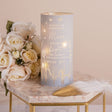 Decorative candle with engraved text next to a bouquet of white roses on a marble surface.