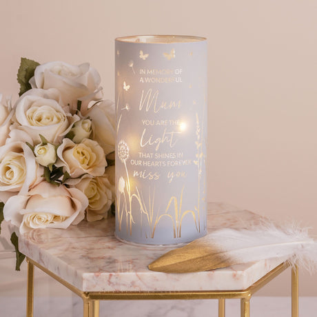 Decorative candle with engraved text next to a bouquet of white roses on a marble surface.