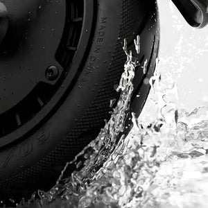 Close-up of black Segway Ninebot electric scooter tire splashing through water, showing textured tread pattern and water droplets in black and white photography