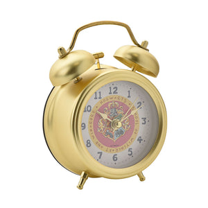 Gold twin bell alarm clock with Hogwarts crest and house emblems on white face with blue numerals, featuring brass finish and metal stand feet