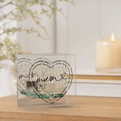 Decorative glass item with 'mum' and heart design on a wooden surface with a blurred candle and plant in the background.