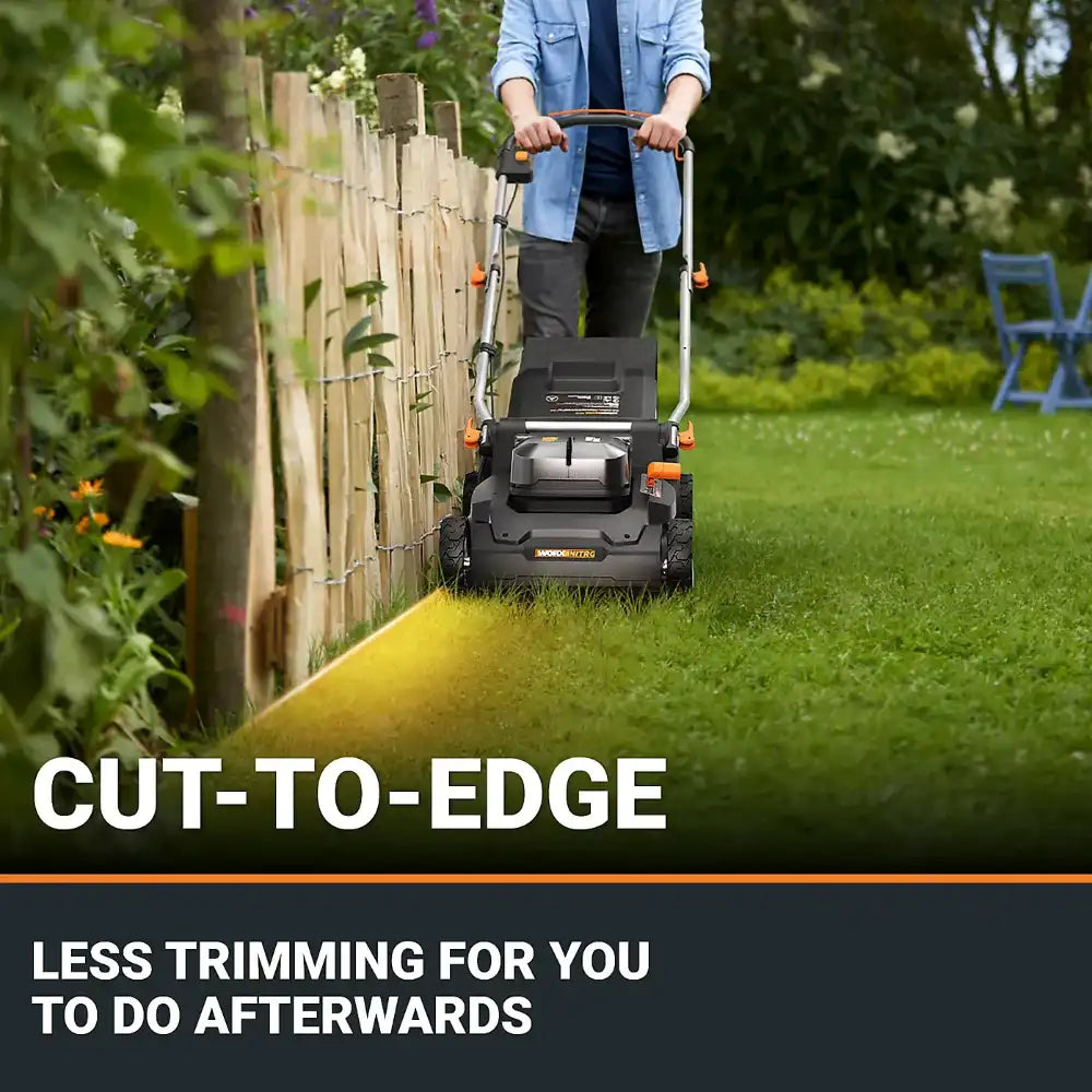 Person operating Worx WG745E 40V cordless lawnmower with cut-to-edge feature along wooden garden fence, demonstrating neat grass trimming capability with yellow cutting line visible on green lawn